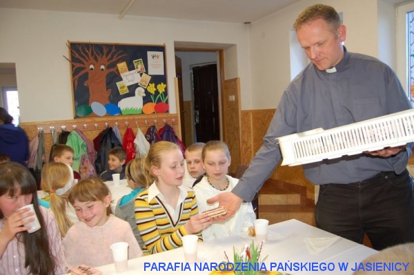Ksiądz Proboszcz rozdaje dzieciom słodkie niespodzianki- mazurki, tradycyjne wielkanocne ciasto